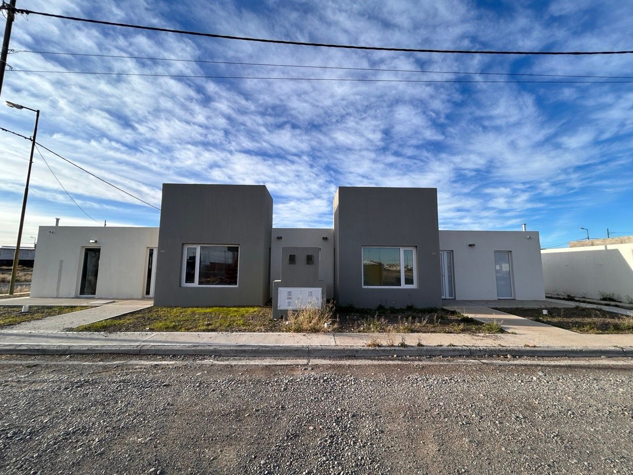 Frente de la casa: volúmenes grises y blancos de una planta, vistos desde la calle bajo un cielo con nubes