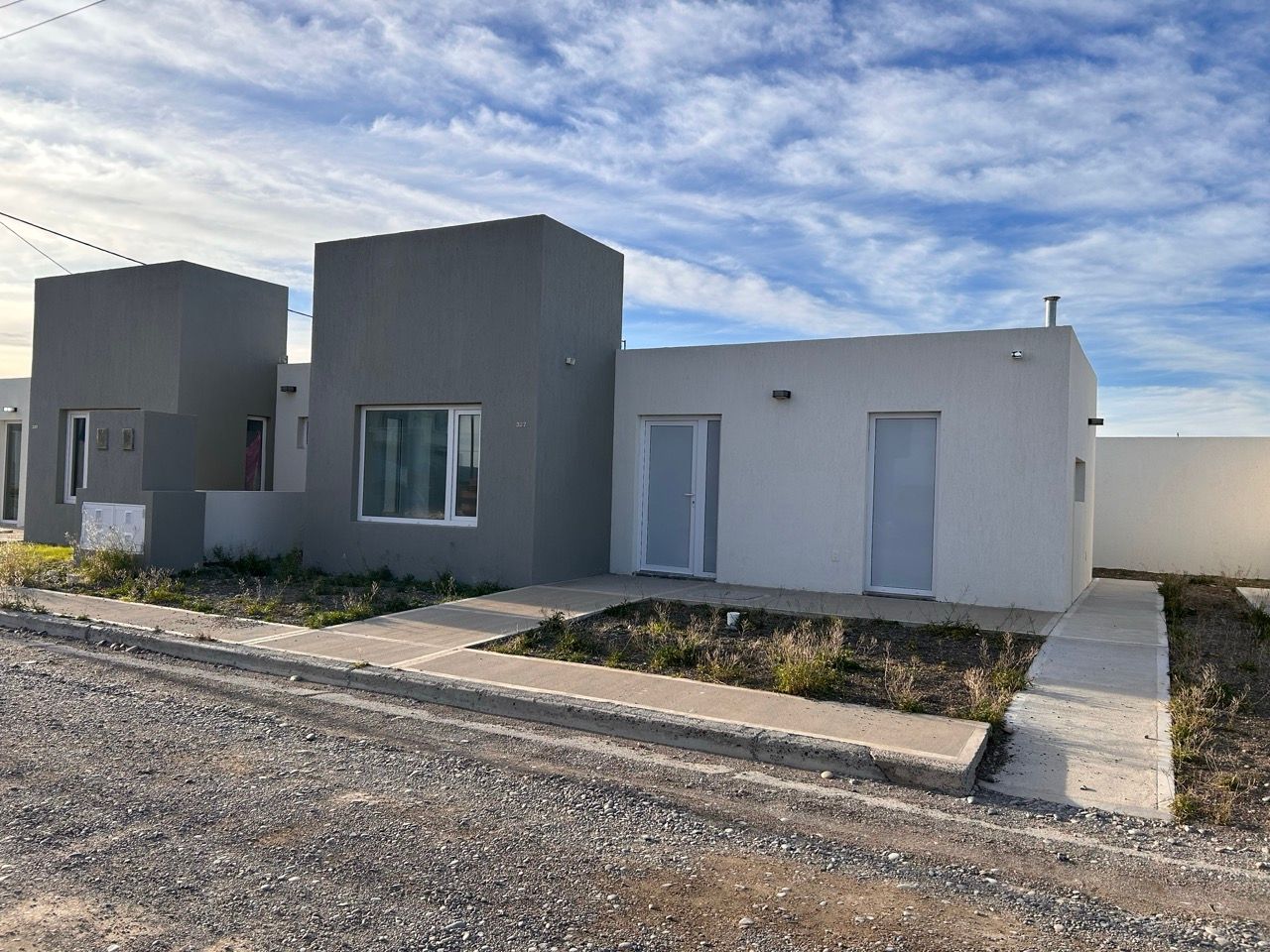 Costado de la casa con vereda de hormigón y jardín al frente