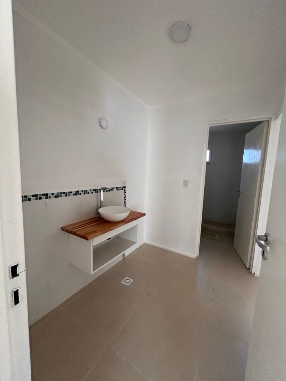 Baño con bacha sobre mesada de madera y piso cerámico