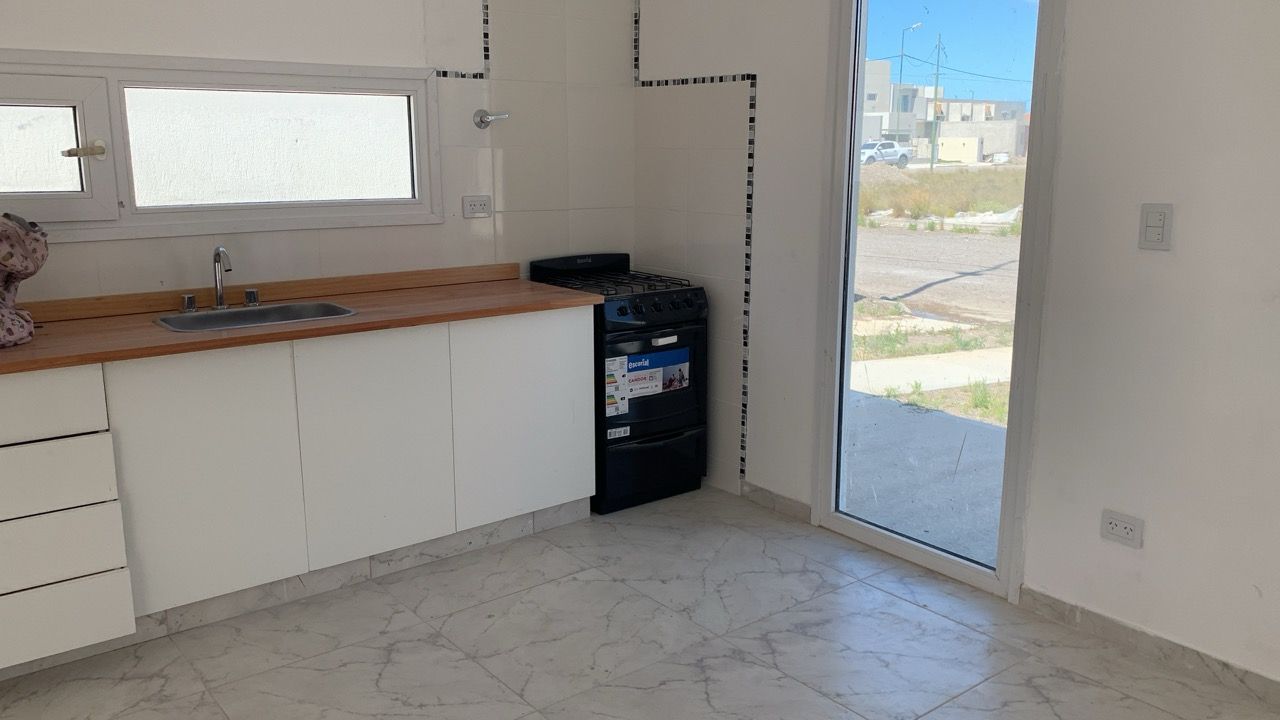 Cocina con muebles blancos, mesada de madera, anafe y puerta vidriada al exterior