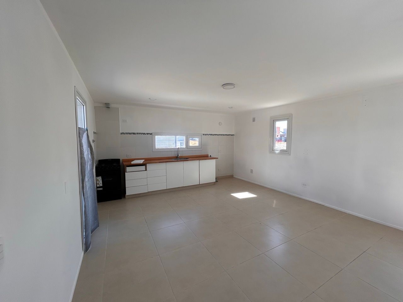 Living y cocina integrados, con mesada de madera, piso cerámico claro y ventanas